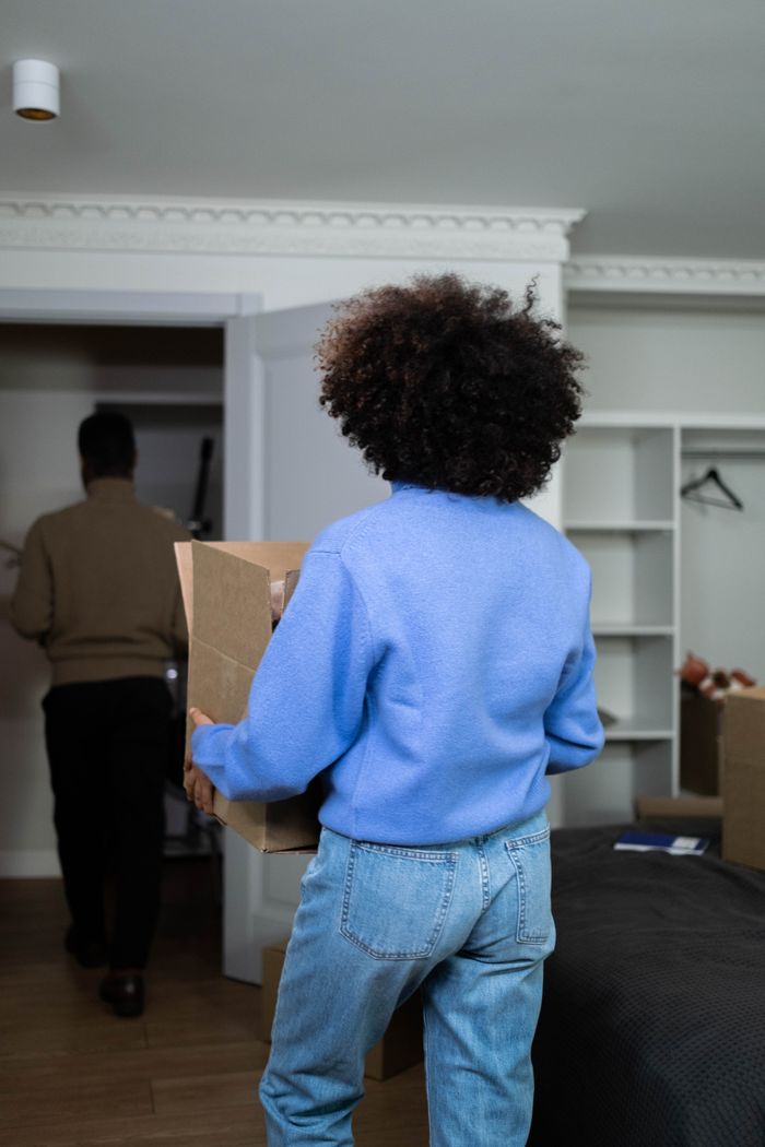 Back view of a woman carrying a box inside a house on moving day, highlighting the idea of moving and relocation.